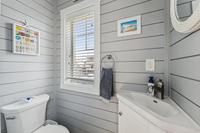 bathroom with toilet, wooden walls, and vanity