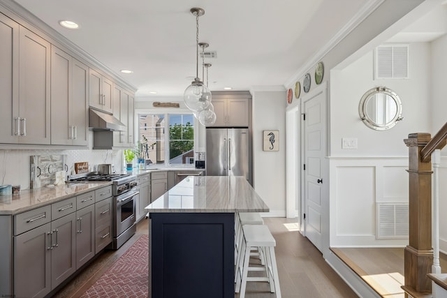 kitchen with premium appliances, light stone counters, hanging light fixtures, and a center island