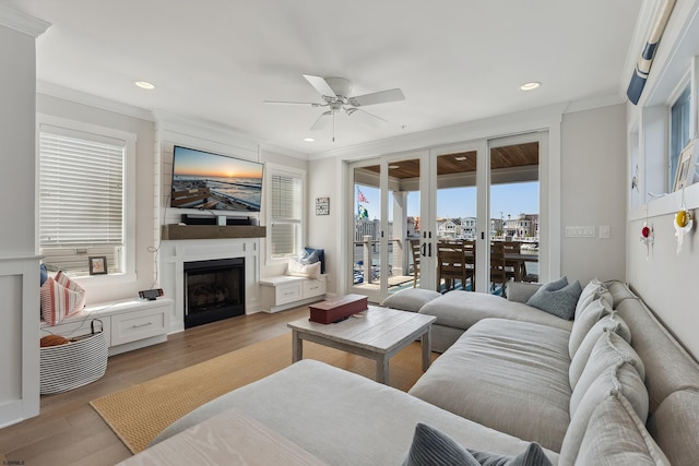 living room featuring ceiling fan, light wood-type flooring, a large fireplace, french doors, and ornamental molding