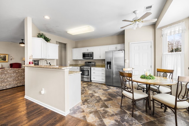 kitchen with ceiling fan, kitchen peninsula, stainless steel appliances, white cabinets, and light stone counters