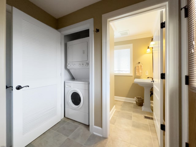 laundry room featuring light tile patterned floors, stacked washer and clothes dryer, and sink