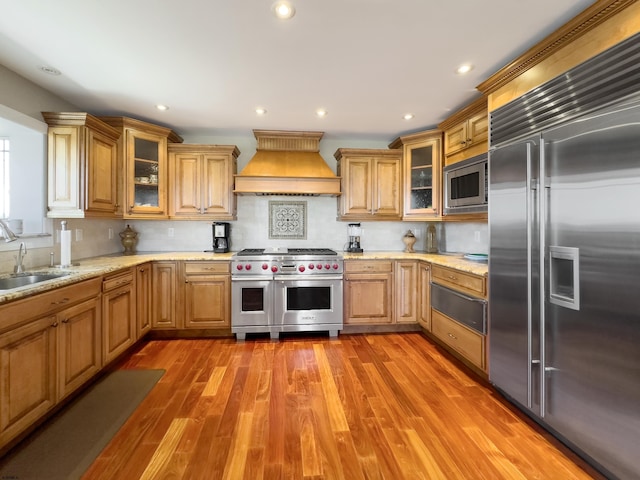 kitchen with premium range hood, hardwood / wood-style floors, backsplash, built in appliances, and sink