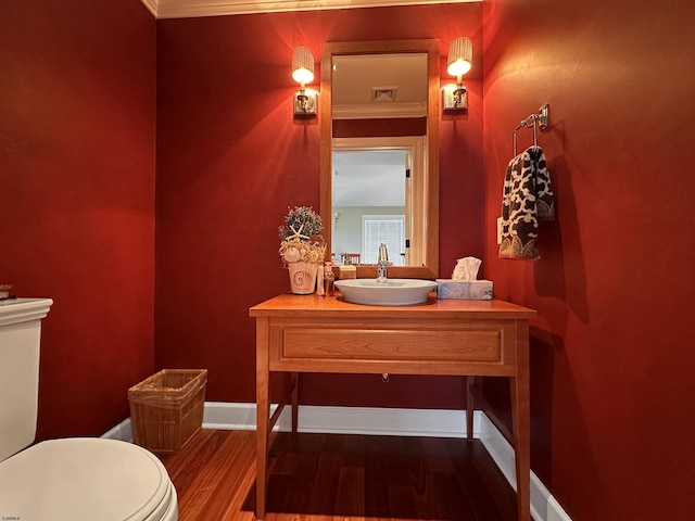 bathroom featuring wood-type flooring, toilet, vanity, and ornamental molding