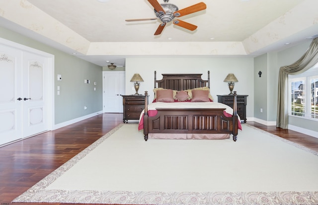 bedroom with dark wood-type flooring, ceiling fan, a closet, and a raised ceiling