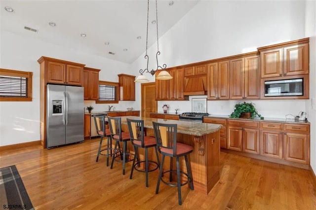 kitchen with a center island, stainless steel appliances, hanging light fixtures, high vaulted ceiling, and a breakfast bar area