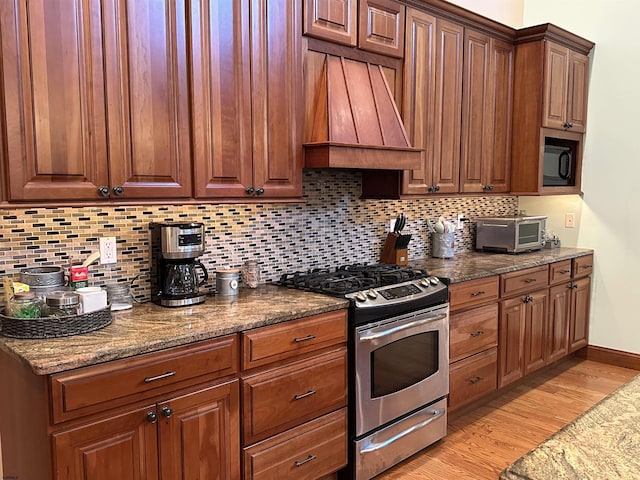 kitchen featuring gas stove, tasteful backsplash, light hardwood / wood-style floors, premium range hood, and dark stone countertops