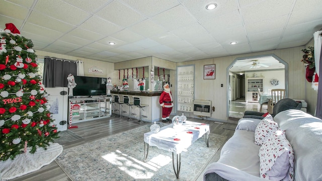 living room featuring dark wood-type flooring, heating unit, a drop ceiling, and ceiling fan