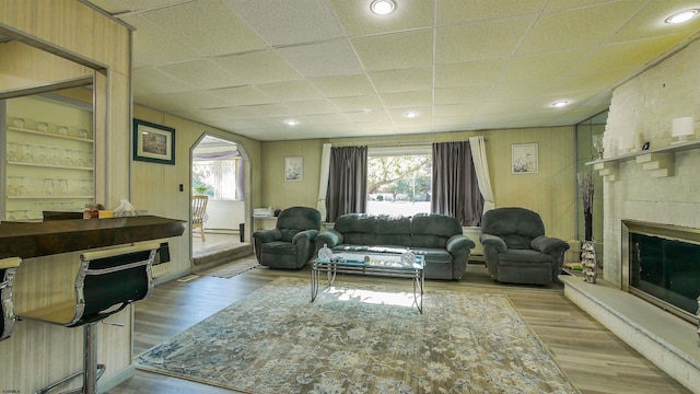 living room featuring light hardwood / wood-style floors, a paneled ceiling, wood walls, and a fireplace