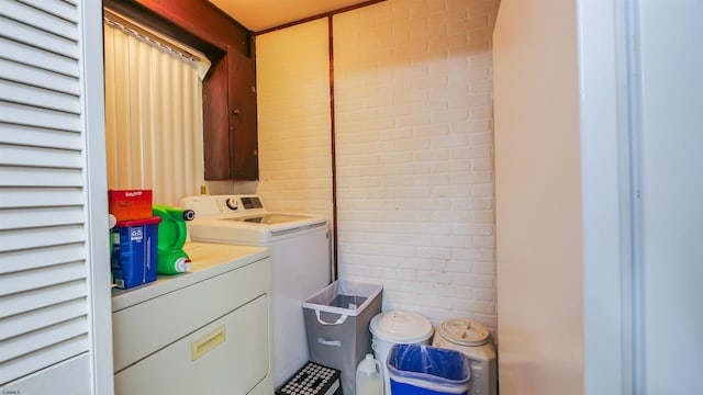 laundry area with brick wall and washing machine and clothes dryer