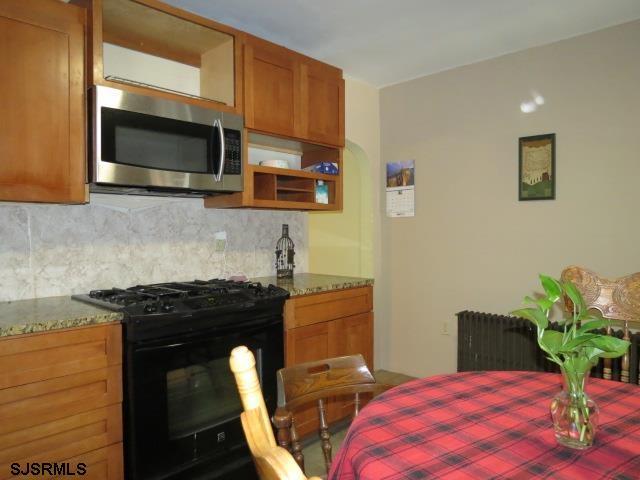 kitchen with decorative backsplash, black gas stove, radiator heating unit, and stone countertops