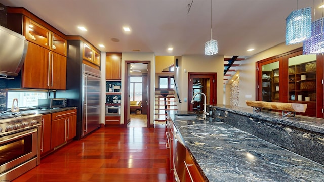 kitchen featuring dark stone countertops, pendant lighting, sink, high end appliances, and dark wood-type flooring