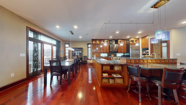 kitchen featuring decorative light fixtures, a kitchen breakfast bar, dark hardwood / wood-style flooring, built in fridge, and dark stone counters