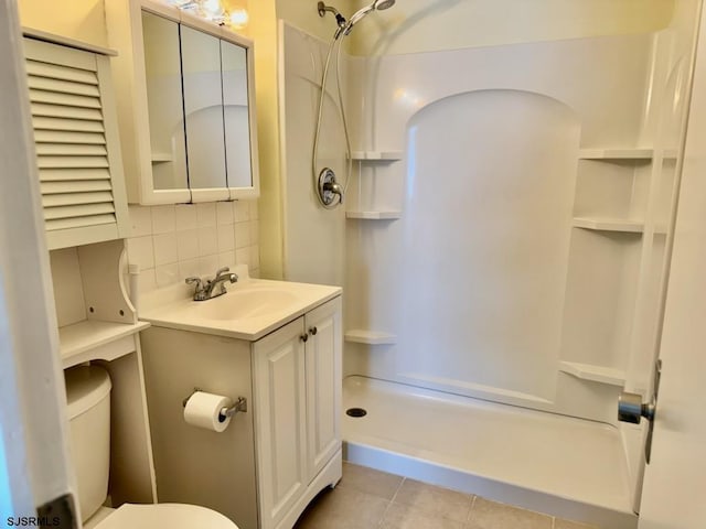 bathroom with backsplash, toilet, vanity, tile patterned flooring, and walk in shower