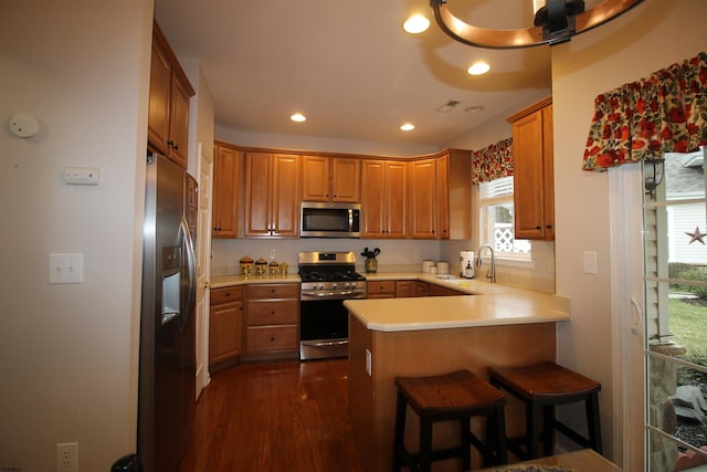 kitchen featuring sink, appliances with stainless steel finishes, a kitchen breakfast bar, dark hardwood / wood-style floors, and kitchen peninsula