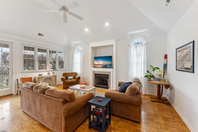 living room featuring ceiling fan, light hardwood / wood-style flooring, a tiled fireplace, and high vaulted ceiling