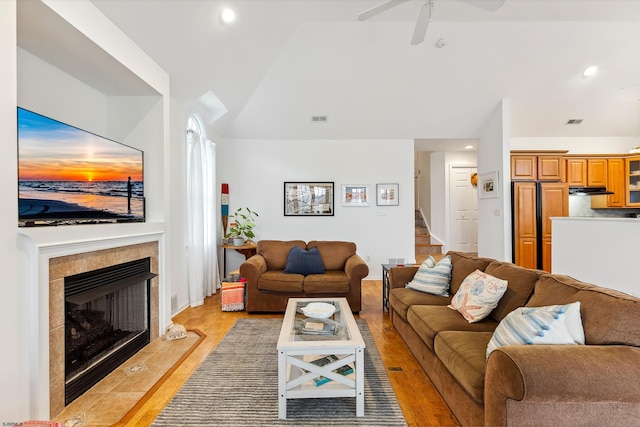 living room featuring ceiling fan, light hardwood / wood-style flooring, lofted ceiling, and a tiled fireplace