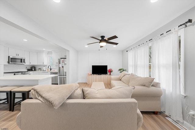 living room featuring ceiling fan, light hardwood / wood-style floors, and sink