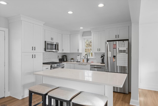 kitchen with white cabinetry, appliances with stainless steel finishes, light wood-type flooring, a kitchen island, and sink