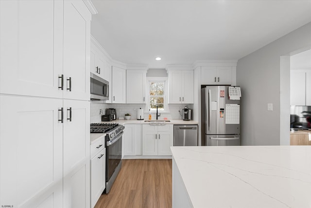 kitchen with backsplash, light hardwood / wood-style floors, sink, appliances with stainless steel finishes, and white cabinets