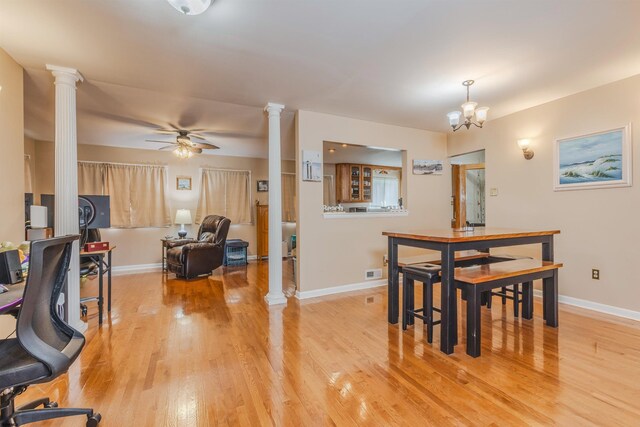 dining space featuring light wood-type flooring, ceiling fan with notable chandelier, and ornate columns