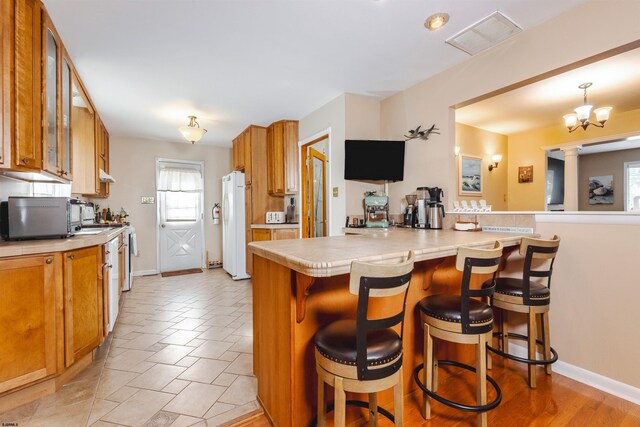 kitchen featuring ornate columns, range with electric cooktop, kitchen peninsula, and a breakfast bar