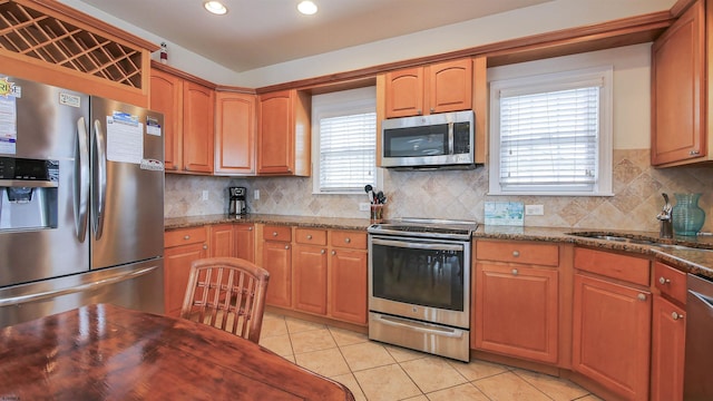 kitchen with a sink, dark stone countertops, light tile patterned flooring, and stainless steel appliances