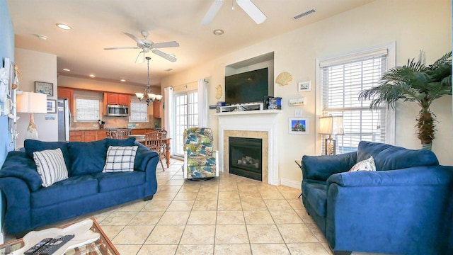 living area featuring light tile patterned floors, visible vents, recessed lighting, a tiled fireplace, and ceiling fan with notable chandelier