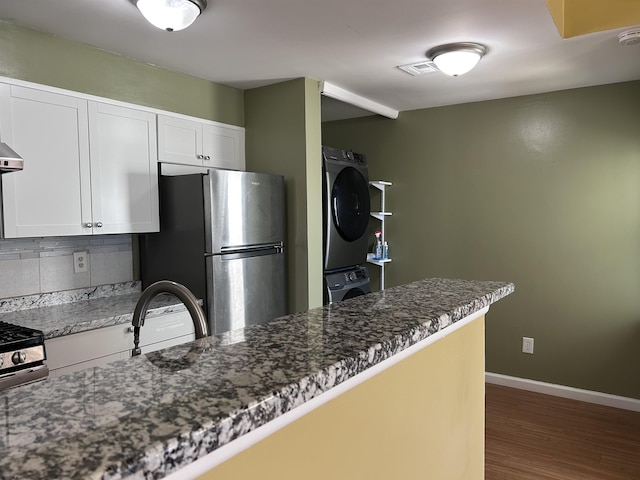 kitchen with appliances with stainless steel finishes, white cabinetry, dark stone countertops, backsplash, and stacked washing maching and dryer