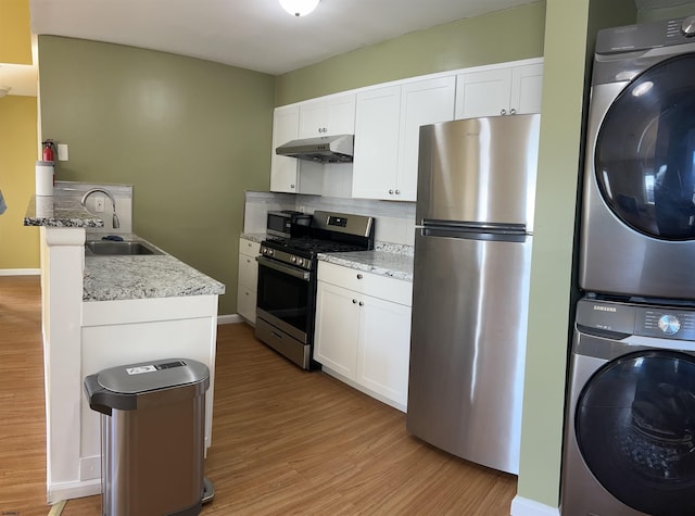 kitchen featuring appliances with stainless steel finishes, white cabinets, sink, light hardwood / wood-style flooring, and stacked washing maching and dryer