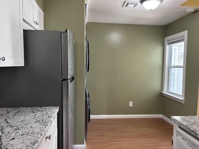 kitchen featuring white dishwasher, white cabinets, light wood-type flooring, light stone counters, and stainless steel refrigerator