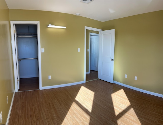 unfurnished bedroom featuring dark wood-type flooring, a closet, and a walk in closet