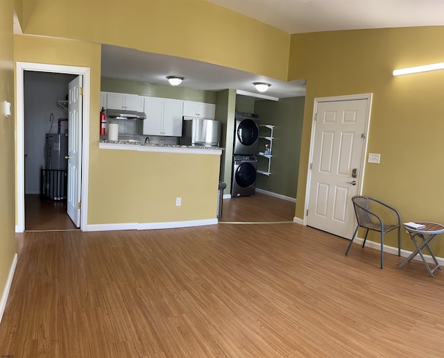 kitchen featuring stainless steel fridge, backsplash, white cabinets, light wood-type flooring, and stacked washer and dryer