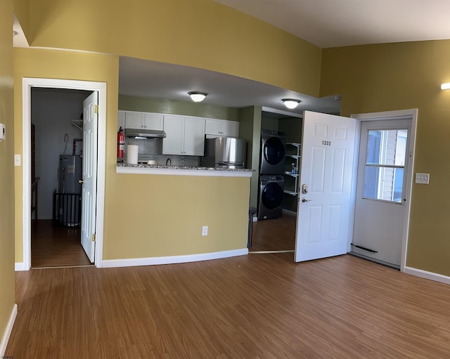 kitchen with hardwood / wood-style flooring, stainless steel refrigerator, white cabinets, stacked washer / dryer, and backsplash