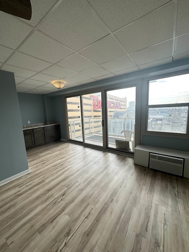 spare room with light hardwood / wood-style floors, a drop ceiling, and a wall unit AC