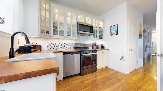 kitchen featuring sink, stainless steel appliances, white cabinets, decorative backsplash, and light wood-type flooring