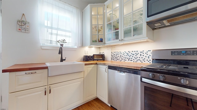 kitchen with sink, butcher block countertops, white cabinetry, light hardwood / wood-style flooring, and stainless steel appliances