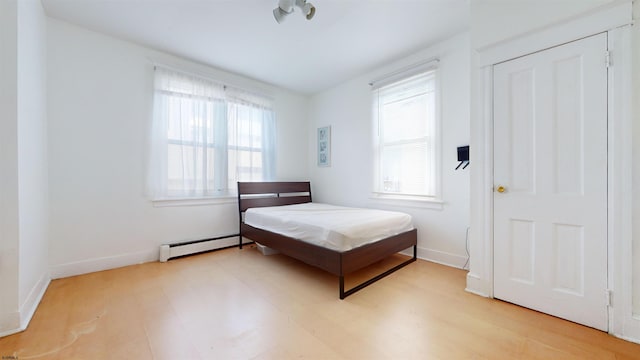 bedroom featuring multiple windows, light hardwood / wood-style floors, and baseboard heating