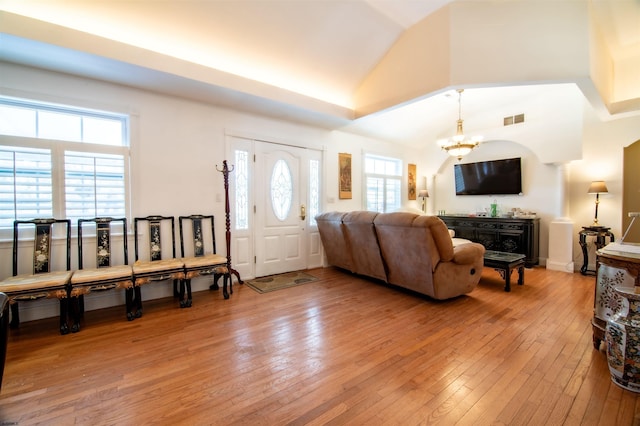 living room featuring high vaulted ceiling, light hardwood / wood-style floors, and a notable chandelier