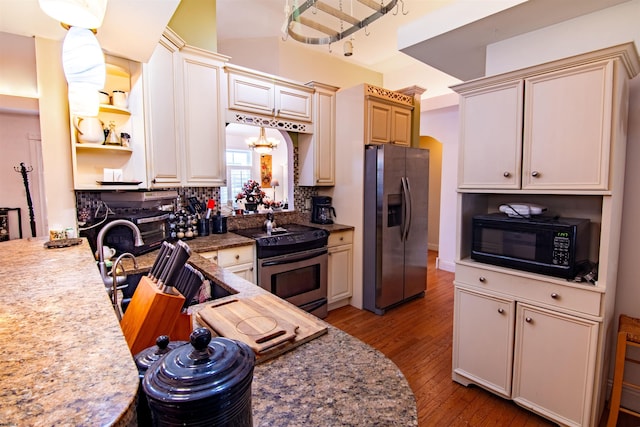 kitchen featuring light hardwood / wood-style flooring, appliances with stainless steel finishes, tasteful backsplash, decorative light fixtures, and cream cabinetry