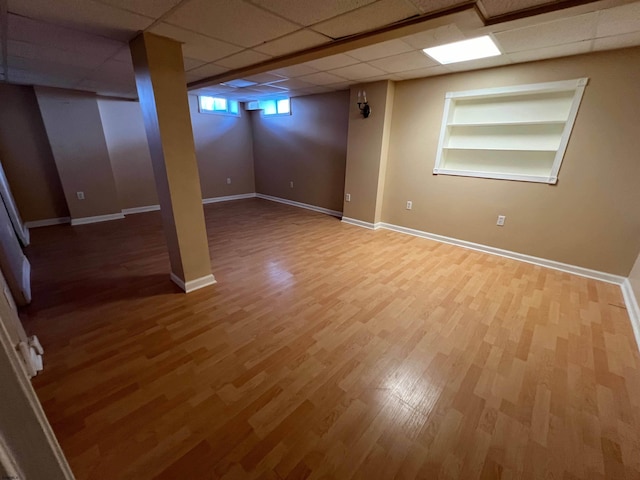 basement featuring hardwood / wood-style flooring, a paneled ceiling, and built in shelves