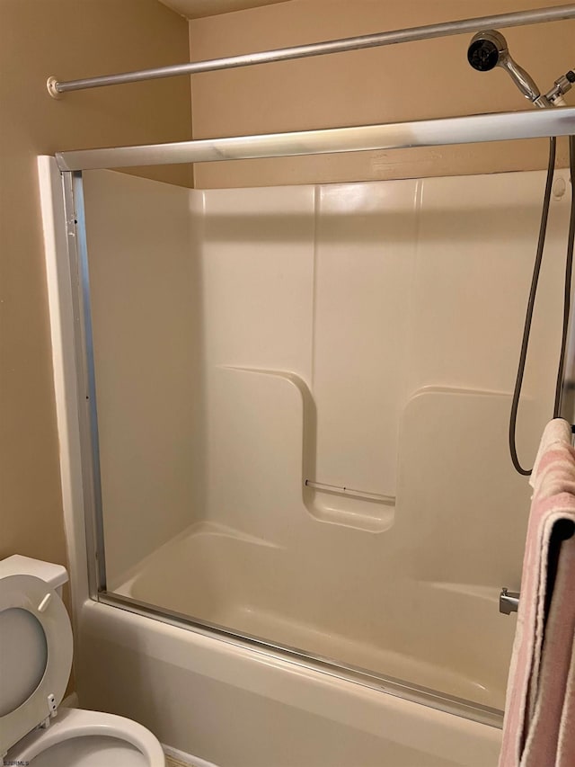 bathroom featuring toilet and bath / shower combo with glass door