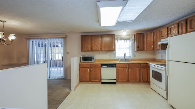 kitchen featuring pendant lighting, sink, white appliances, a notable chandelier, and a textured ceiling