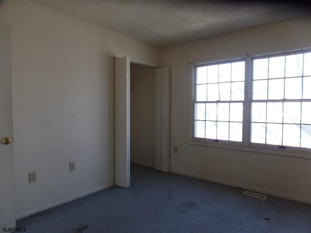 unfurnished bedroom with a textured ceiling, carpet flooring, visible vents, and baseboards