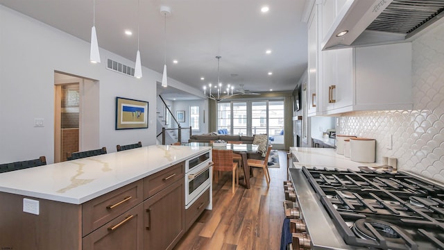 kitchen featuring premium range hood, hanging light fixtures, dark hardwood / wood-style flooring, cooktop, and oven