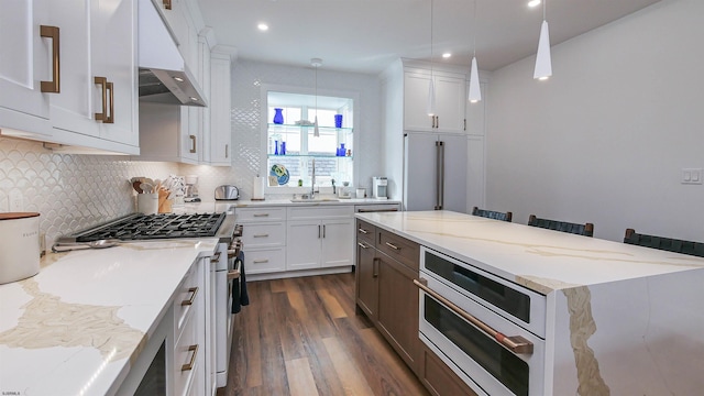 kitchen with white cabinetry, hanging light fixtures, premium appliances, custom range hood, and light stone countertops