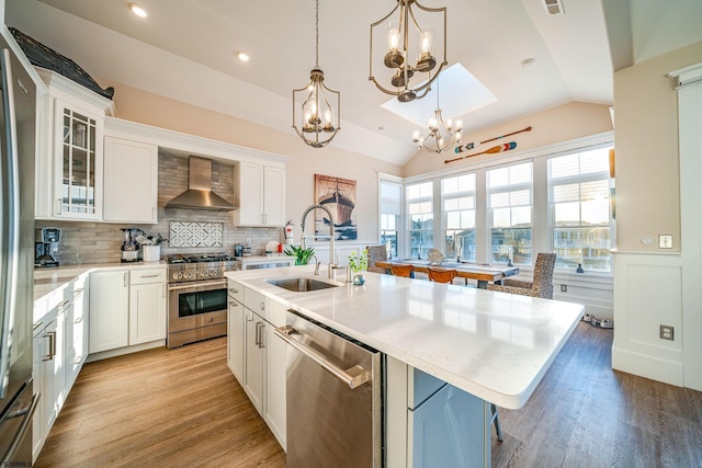 kitchen featuring lofted ceiling, sink, appliances with stainless steel finishes, a kitchen island with sink, and wall chimney exhaust hood