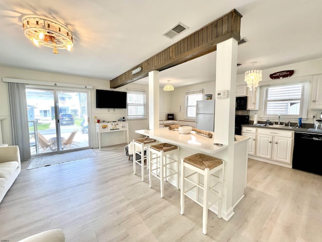 kitchen featuring decorative light fixtures, a breakfast bar area, white cabinets, light hardwood / wood-style floors, and black appliances