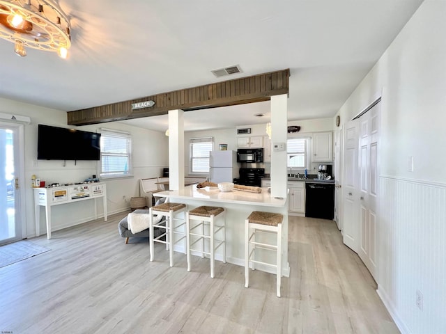 kitchen with black appliances, a breakfast bar, light wood-type flooring, and white cabinets