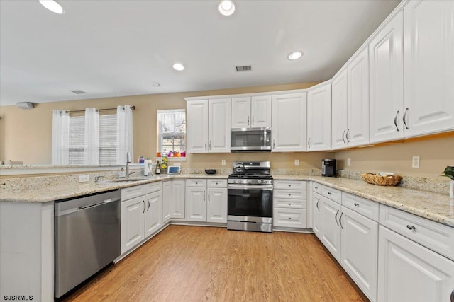 kitchen featuring visible vents, white cabinets, stainless steel appliances, light wood-style floors, and a sink