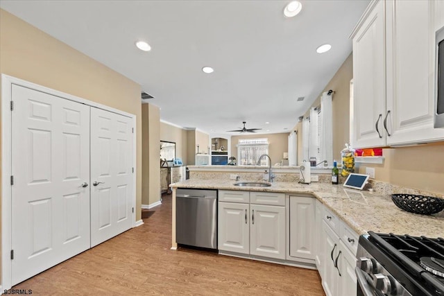 kitchen featuring stainless steel appliances, a peninsula, a sink, white cabinetry, and light wood-style floors